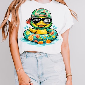 Peut inclure: Un t-shirt blanc avec un motif représentant un canard jaune portant une casquette verte à motifs de palmiers et des lunettes de soleil noires. Le canard est dans une bouée turquoise décorée de tranches d'orange et de glaces, avec le texte SUMMER VIBES.