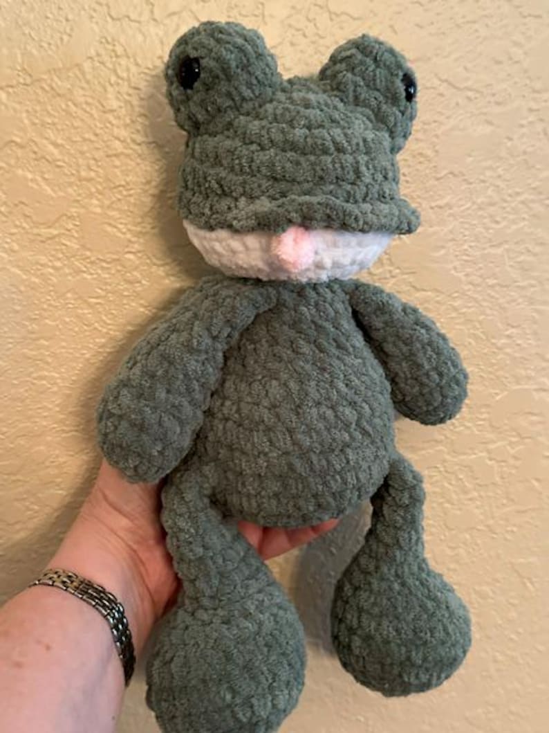 Puede incluir: Un juguete de rana de peluche hecho a mano en tonos verdes, blancos y rosas. La rana tiene ojos grandes y redondos, una barriga blanca y una boca rosa. El material suave y texturizado le da a la rana una apariencia achuchable. Un art&iacute;culo encantador, hecho a mano.