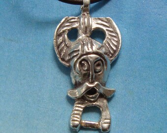 May include: A silver pendant necklace with a detailed design of a face with a mustache and a helmet. The pendant is attached to a black leather cord.
