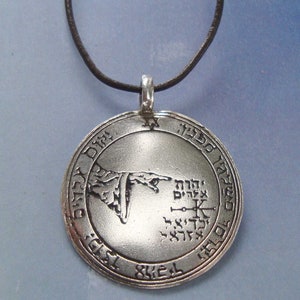 May include: A silver pendant necklace with a circular pendant featuring a hand pointing to a symbol with Hebrew text. The pendant is on a black leather cord.