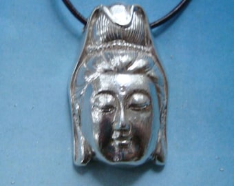 May include: Silver pendant necklace featuring a detailed depiction of a Buddha's face. The pendant is attached to a black leather cord.