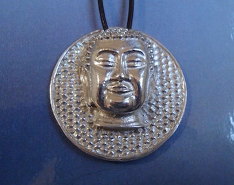 May include: Silver pendant necklace featuring a detailed Buddha head with closed eyes. The pendant is round and has a textured background.