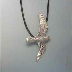 Könnte beinhalten: Silberne Halskette mit Anhänger, der einen detaillierten, stilisierten Falken im Flug zeigt. Der Anhänger ist an einem schwarzen Lederband befestigt.