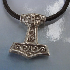May include: Silver Mjolnir pendant with intricate details, including a face on the top, on a black leather cord.
