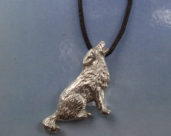 May include: Silver wolf pendant necklace with a detailed design, howling at the moon. The pendant is on a brown leather cord.