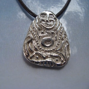 Puede incluir: Collar con colgante de plata que presenta una cara estilizada detallada con una expresión sonriente. El colgante tiene forma de lágrima y tiene diseños intrincados alrededor de la cara.