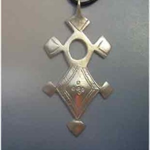 May include: A silver-colored pendant in the shape of a cross. The pendant has a circular opening in the center and diamond-shaped accents at the ends of the cross arms. The pendant hangs from a black cord.