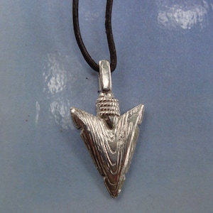 May include: A silver arrowhead pendant on a brown leather cord necklace.