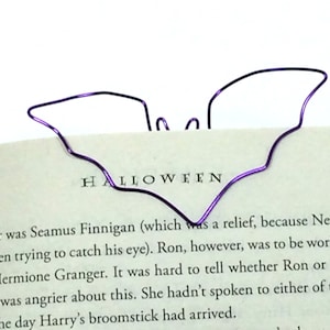May include: A purple wire bat bookmark with the word "HALLOWEEN" printed on a book page.