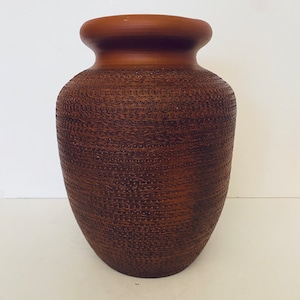 Peut inclure: Un vase en céramique marron avec une surface texturée. Le vase a une base large qui se rétrécit vers le haut jusqu'à un col plus étroit et un bord évasé. Le motif texturé recouvre tout le corps du vase.