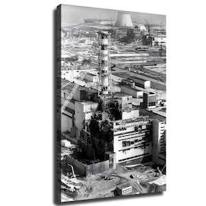 Könnte beinhalten: Eine schwarz-weiße Luftaufnahme des Kernkraftwerks Tschernobyl, die das beschädigte Reaktorgebäude mit einem hohen, gestreiften Abluftkamin, umliegende Industrieanlagen und einen großen Kühlturm in der Ferne zeigt.