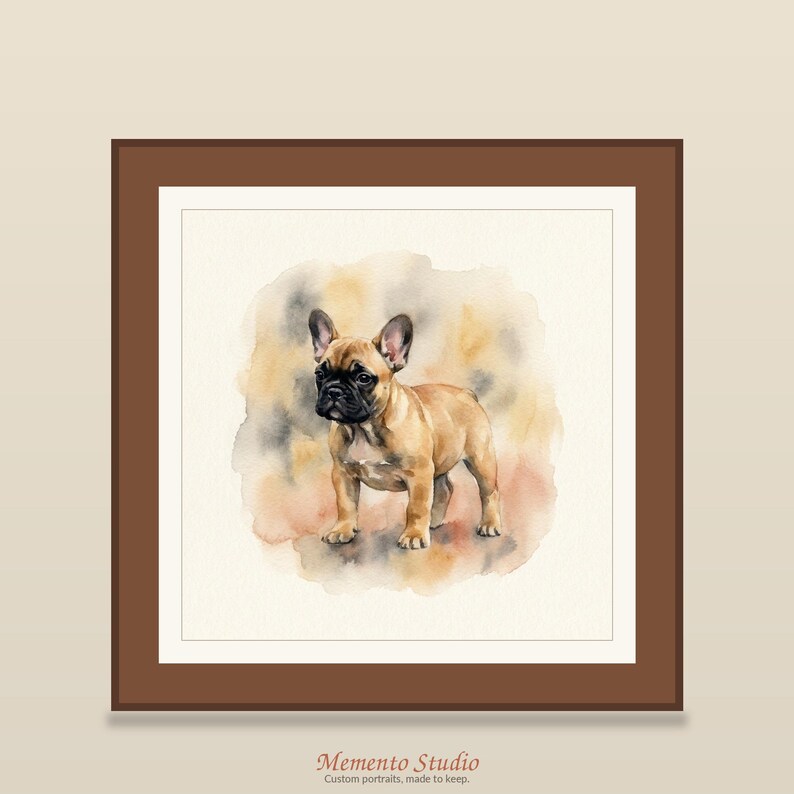 May include: A framed watercolour painting of a fawn French Bulldog with a black muzzle, standing against a soft, blended background of tan, grey, and orange hues. The artwork is enclosed in a simple brown frame with the text Memento Studio below.