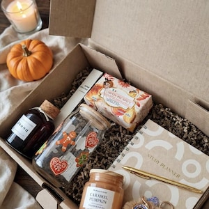 Könnte beinhalten: Eine Geschenkschachtel aus Karton mit einer Glasflasche mit Korken, einem Glas mit Lebkuchenmotiven, einer Pumpkin Pie Spice-Schachtel, einem Caramel Pumpkin-Glas, einem spiralgebundenen Studienplaner, einem goldenen Stift und einem flauschigen Eulen-Schlüsselanhänger.
