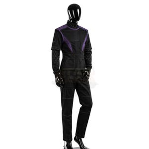 May include: A black and purple long-sleeved tunic and matching trousers set displayed on a mannequin. The tunic features a high collar, purple shoulder panels, and quilted sleeve details. The trousers have visible stitching and a straight-leg cut.