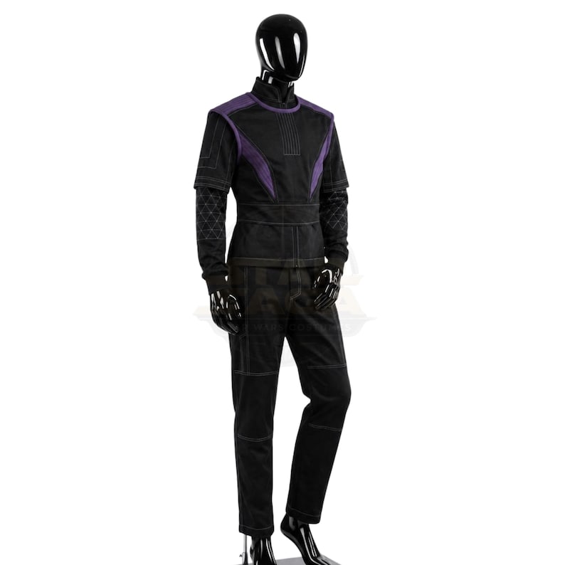 May include: A black and purple long-sleeved tunic and matching trousers set displayed on a mannequin. The tunic features a high collar, purple shoulder panels, and quilted sleeve details. The trousers have visible stitching and a straight-leg cut.