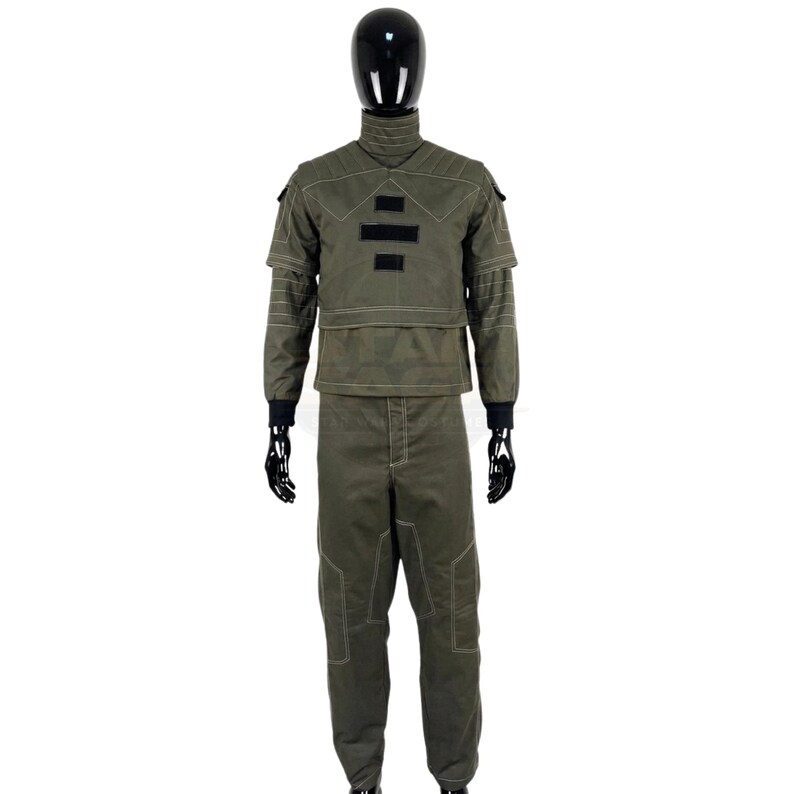 May include: An olive green tactical uniform set consisting of a long-sleeved jacket with a high collar, quilted shoulder panels, and three black rectangular patches on the chest, paired with matching trousers featuring reinforced knee stitching.