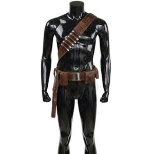 May include: A brown leather bandolier and utility belt set featuring a diagonal shoulder strap with silver-toned cylindrical cartridge holders, a central metallic buckle, two attached rectangular pouches, and a long holster on the right side.