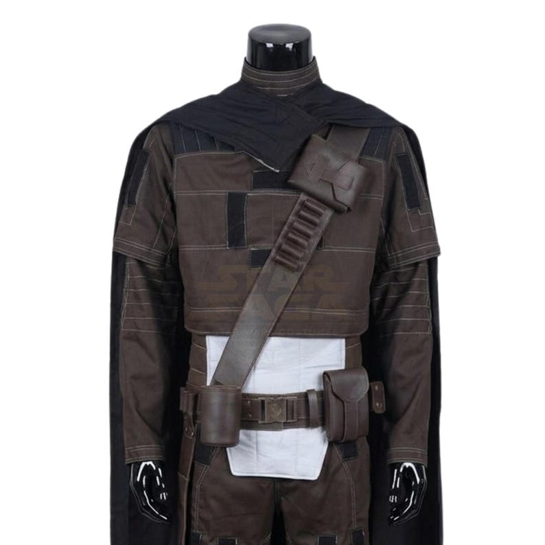 Peut inclure: Un ensemble de costume marron fonc&eacute; et noir comprenant une veste courte avec des coutures horizontales, une cape noire et une ceinture utilitaire marron avec des pochettes et un &eacute;tui. L'ensemble inclut un panneau de taille blanc et une bandouli&egrave;re.