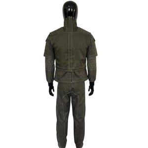 May include: A dark olive green two-piece uniform set featuring a high-collar jacket with white contrast stitching, short sleeves with geometric patterned panels, and matching long trousers. The jacket includes a central vertical zipper closure.