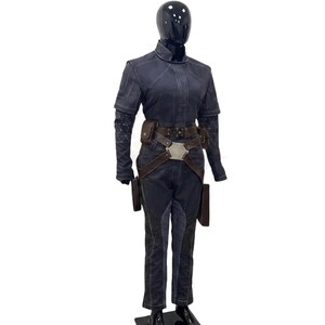 May include: A dark charcoal gray tactical jumpsuit featuring a high collar, short sleeves with geometric patterned under-sleeves, and a brown leather utility belt with a central metallic hexagonal buckle and attached pouches, worn on a black mannequin.