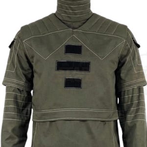 May include: An olive green long-sleeve tactical shirt featuring a high mock neck collar, reinforced shoulder panels with visible white stitching, and three rectangular black hook-and-loop patches centered on the chest area.
