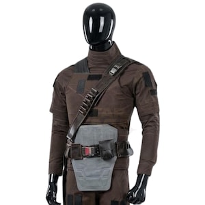 K&ouml;nnte beinhalten: Ein dunkelbraunes taktisches Set aus lang&auml;rmeligem Oberteil und Hose auf einer schwarzen Schaufensterpuppe. Das Outfit umfasst einen dunkelbraunen Schulterriemen mit metallischen Akzenten, eine hellgraue Bauchpanzerplatte und einen G&uuml;rtel mit schwarzer Tasche.