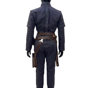 May include: A dark navy blue long-sleeved jumpsuit featuring horizontal stitched detailing on the sleeves and back. The garment is cinched at the waist with a brown leather utility belt that includes a holster attachment on the right side.