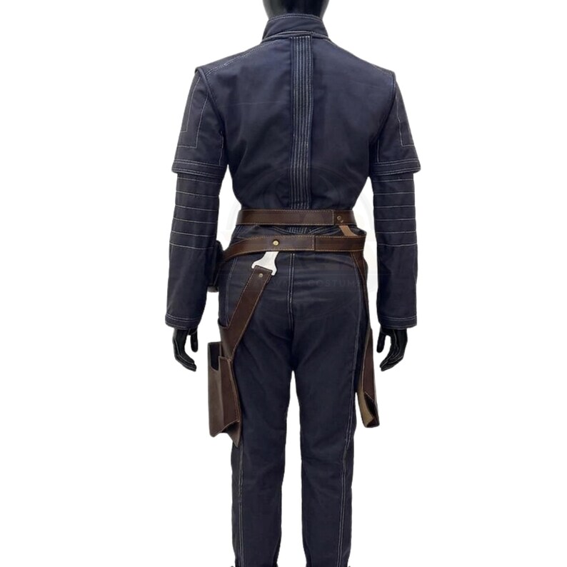 May include: A dark navy blue long-sleeved jumpsuit featuring horizontal stitched detailing on the sleeves and back. The garment is cinched at the waist with a brown leather utility belt that includes a holster attachment on the right side.
