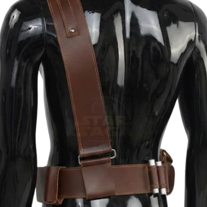May include: A brown leather belt and shoulder strap set featuring a wide waist belt with integrated pouches and a diagonal shoulder strap. The belt includes two silver-colored cylindrical canisters attached to the side and a metal buckle fastener.