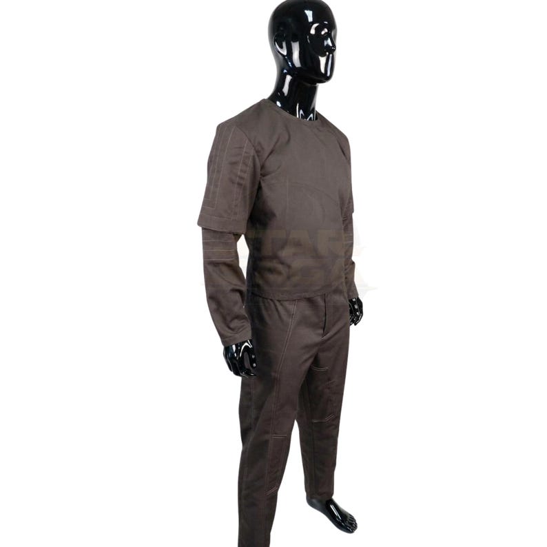 K&ouml;nnte beinhalten: Ein dunkelbraunes Set aus einem lang&auml;rmeligen Oberteil und einer passenden Hose auf einer gl&auml;nzenden schwarzen Schaufensterpuppe. Das Oberteil hat einen Rundhalsausschnitt und strukturierte Eins&auml;tze an den &Auml;rmeln, w&auml;hrend die Hose sichtbare N&auml;hte aufweist.