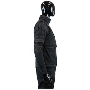 Puede incluir: Una chaqueta de estilo t&aacute;ctico negra con cuello alto, mangas cortas y una superposici&oacute;n de chaleco estructurado. La prenda presenta un patr&oacute;n geom&eacute;trico triangular en las mangas, detalles de parches rectangulares en los hombros y costuras visibles.