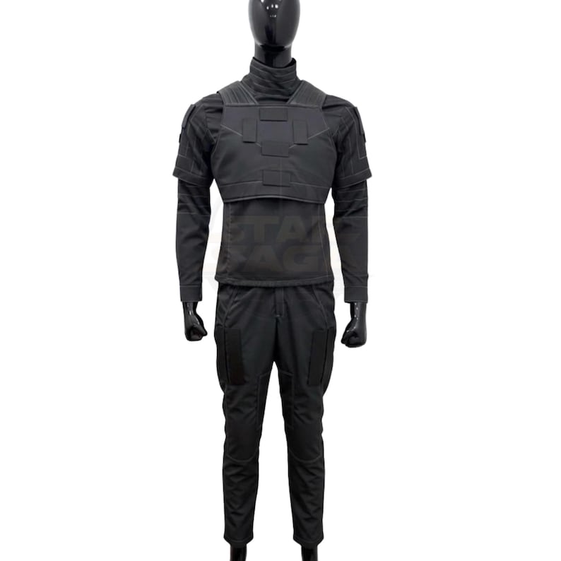 Puede incluir: Un uniforme t&aacute;ctico negro que consiste en una camisa de manga larga con cuello alto, una placa pectoral estructurada con paneles rectangulares y pantalones a juego con grandes bolsillos laterales. El conjunto se muestra sobre un maniqu&iacute; negro.