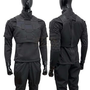 Puede incluir: Un conjunto de uniforme negro de estilo t&aacute;ctico que consta de una camisa de manga larga con cuello alto, una placa pectoral estructurada con parches rectangulares y pantalones a juego. Las mangas presentan un patr&oacute;n geom&eacute;trico de tri&aacute;ngulos.