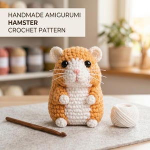 May include: A handmade amigurumi hamster crochet pattern featuring a small, stuffed hamster toy with golden-brown and white yarn, black plastic eyes, and white whiskers. A wooden crochet hook and a small ball of white yarn sit beside the hamster.