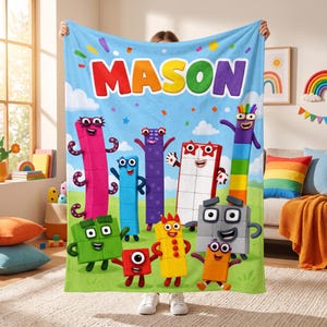 May include: A light blue fleece blanket featuring the name MASON in large, colorful letters at the top. The design includes various Numberblocks characters in red, green, blue, yellow, purple, and grey, set against a green grassy field.
