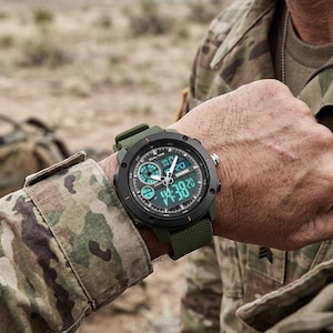 May include: A tactical wristwatch with a matte black circular bezel and a textured olive green silicone strap. The watch face features a dual analog and digital display with the brand name Skmei printed in white, showing a time of 14:38.