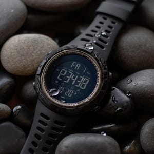 May include: A black digital sports watch with a round face, a textured silicone strap, and a dark display showing the time 2:34:38, the date 10-20, and the day FA 1. The watch features a rugged bezel and is covered in small water droplets.