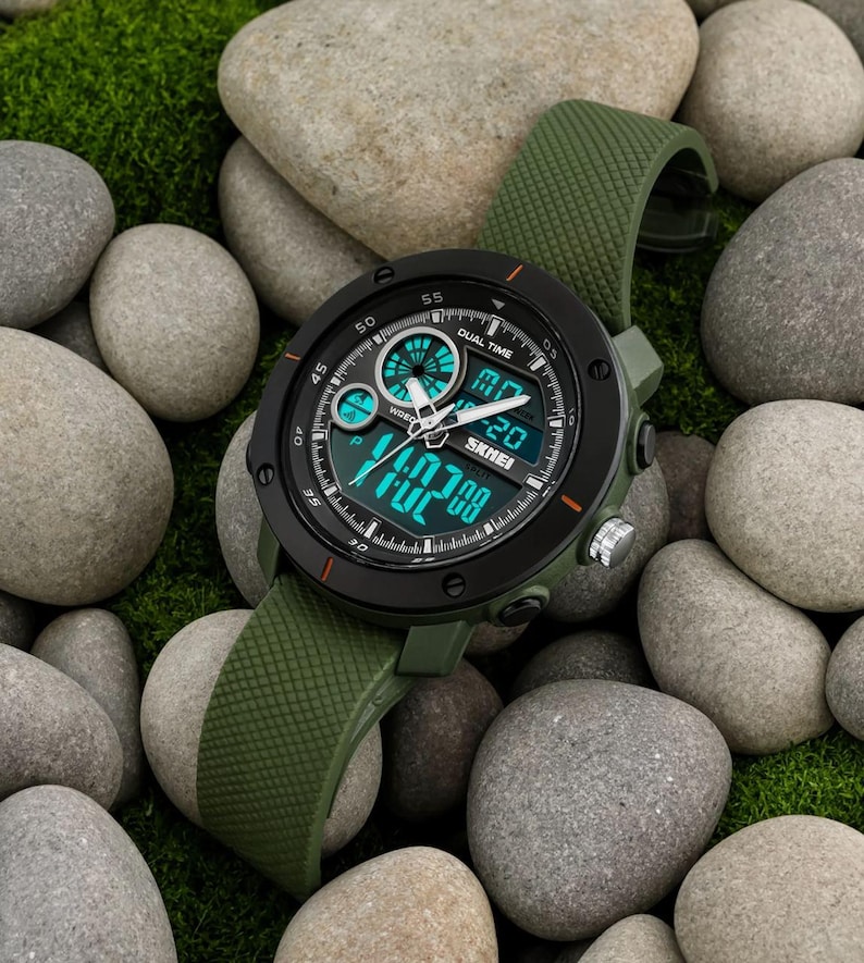 May include: A round analog-digital wristwatch with a matte black bezel and an olive green textured silicone strap. The watch face features a black background with bright teal digital displays, white hour and minute hands, and the brand name SKMEI.