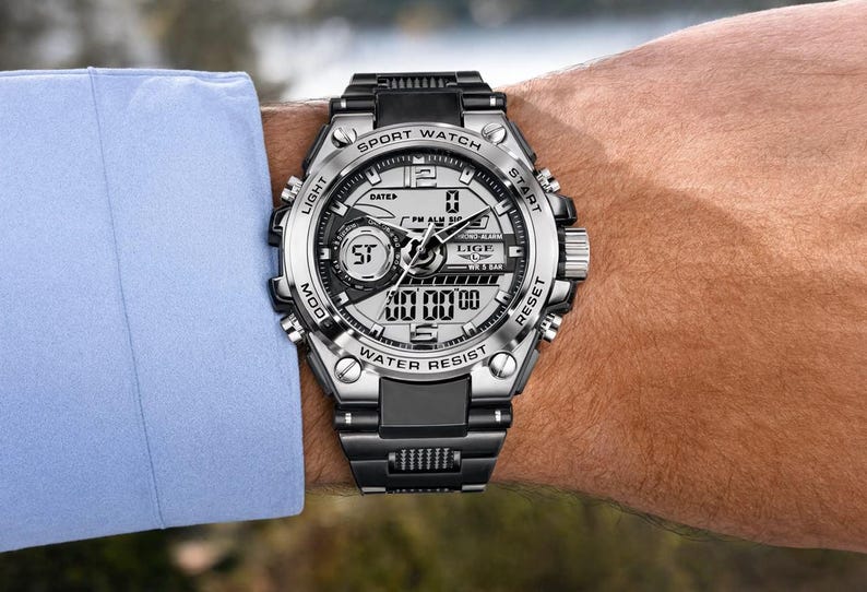 May include: A silver and black analog-digital sport watch with a metallic bezel, featuring the text LIGE, SPORT WATCH, WATER RESIST, LIGHT, START, MOD, and RESET. The watch has a multi-functional dial with digital displays and a black link band.