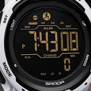 May include: A white digital sports watch with a black circular face featuring gold-colored digital numbers and text. The display shows the time 7:43:08, along with icons for a runner, battery level, and labels including ALM, CHIME, KCAL, DIST, KM, KG, MILE, LB, IN, and SAMDA.