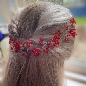 Peut inclure: Une vigne de cheveux perlée rouge, avec un design floral délicat. L'accessoire pour cheveux est fabriqué avec de petites perles rouges vives et du fil d'argent, créant un look étincelant et élégant. La vigne est montrée dans une coiffure.