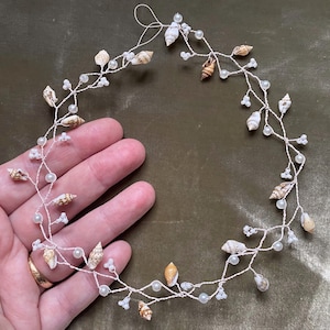 May include: A delicate silver wire headband adorned with small white pearls and seashells. The headband is perfect for a beach wedding or a summer party.