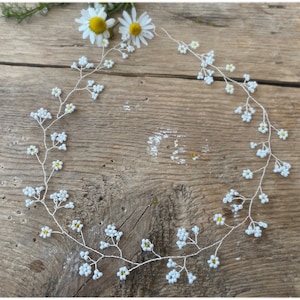 以下が含まれることがあります： 小さな白い花と黄色の芯を持つ、繊細な白い花のヘアバイン。つるはワイヤー製で柔軟性があり、形やスタイルを簡単に変えられます。