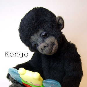May include: A black plush gorilla toy holding a yellow, green, red, and blue plastic baby teether. The toy is labeled "Kongo".