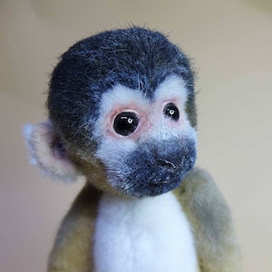 以下が含まれることがあります： 茶色の毛皮、白い胸、黒い顔をしたぬいぐるみのおさるさん。おさるさんは大きく黒い目を持ち、好奇心旺盛な表情をしています。