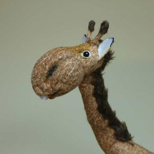 以下が含まれることがあります： 耳に白いパッチが付いた茶色と黒のぬいぐるみキリンのクローズアップ。キリンは長い首と長い鼻を持つ大きな頭をしています。