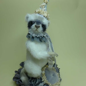 以下が含まれることがあります： 黒目の白いぬいぐるみが、青と白のパーティーハットをかぶり、グレーと白の布製のクッションに座っている。