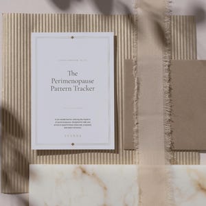 Può includere: Un libretto di tracciamento rettangolare bianco intitolato The Perimenopause Pattern Tracker con linee di bordo e testo dorati. La copertina include il sottotitolo A six-month tool for noticing the rhythms of perimenopause e il marchio YVENNE.