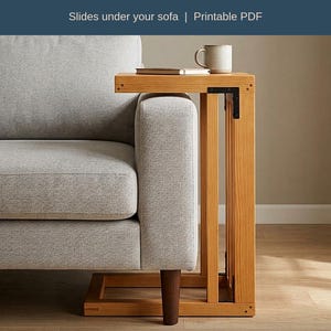 Puede incluir: Una mesa auxiliar en forma de C de madera clara con esquinas reforzadas en acero negro. La mesa está junto a un sofá gris y sostiene un pequeño cuaderno y una taza de cerámica. El texto dice: C Side Table Plans, Slides under your sofa, Printable PDF, Steel-braced corners, Inch + mm, Fits-your-sofa guide.