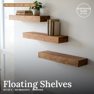 May include: Three rectangular wooden floating shelves mounted in a staggered arrangement on a wall. The top shelf holds two books and a small potted plant. The middle shelf holds three books. The text reads PDF PLAN, CUT LIST, INCH + CM, HEARTWOOD PLANS EST 2026, and Floating Shelves SET OF 3 NO BRACKETS BEGINNER.